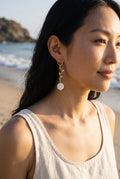 Sand and Sea 18k gold dangle earrings with white shell bead and crystal leaf accents. Coastal elegance.