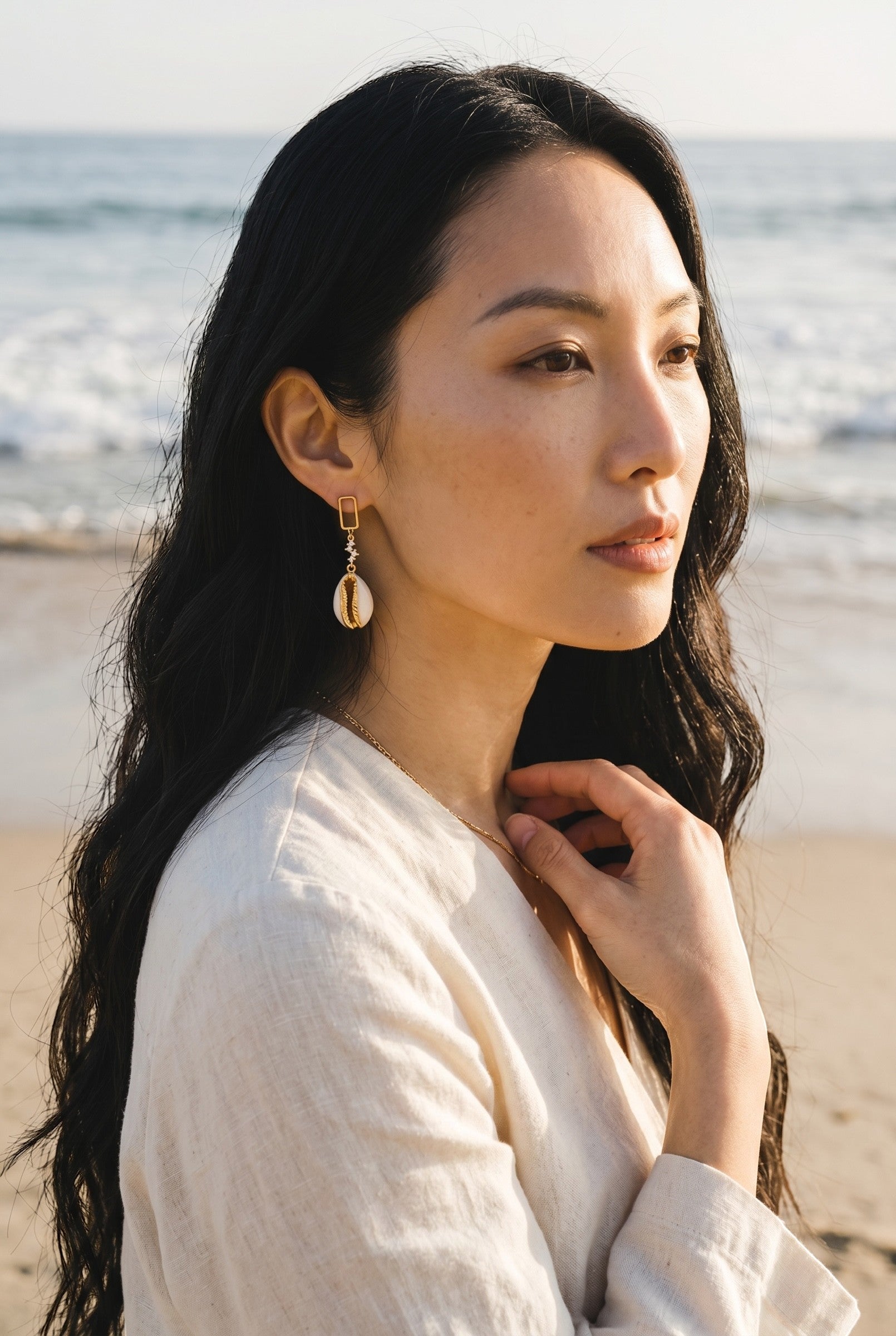 Sand and Sea gold-tone dangle earrings with cubic zirconia stud and natural cowrie shell pendant.