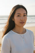 Sand and Sea engraved silver vertical bar necklace on a woman at the beach. Stainless steel pendant with laser etching.