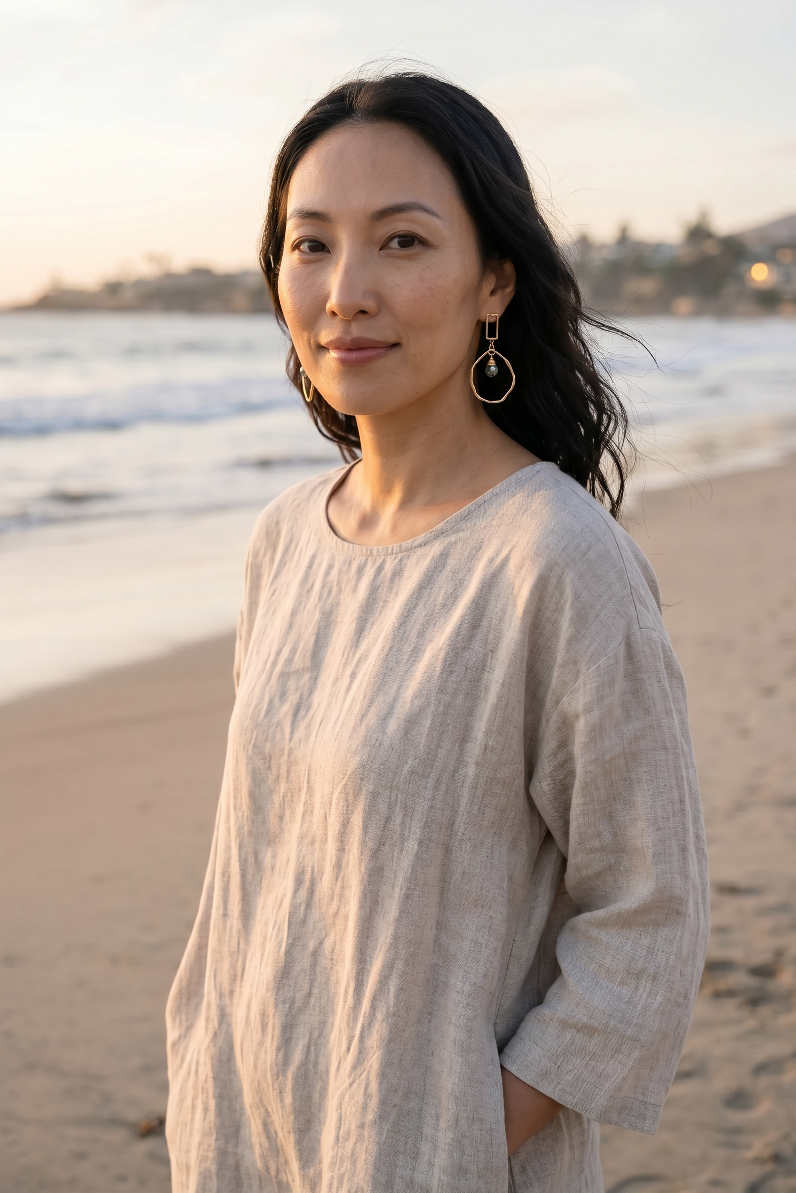 Sand and Sea geometric gold-tone drop earrings with pyrite stone accent, worn by a woman on a beach.