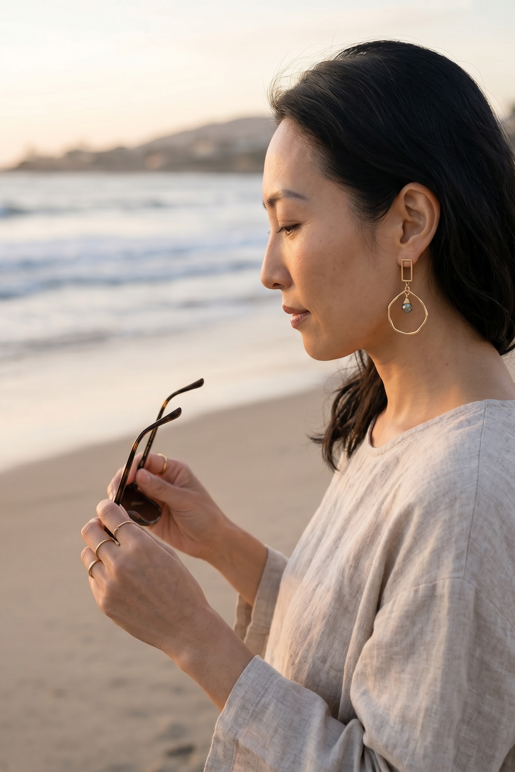 Sand and Sea geometric gold-tone drop earrings with pyrite stone accent, worn by a woman on the beach.