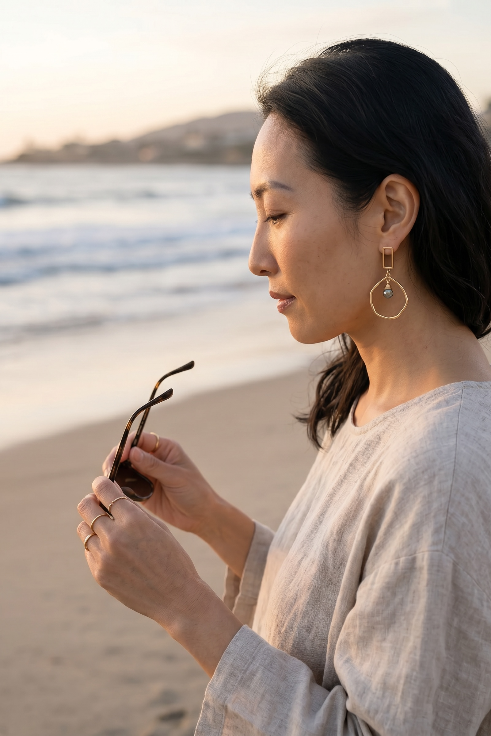 Sand and Sea geometric gold-tone drop earrings with pyrite stone accent, worn by a woman on the beach.