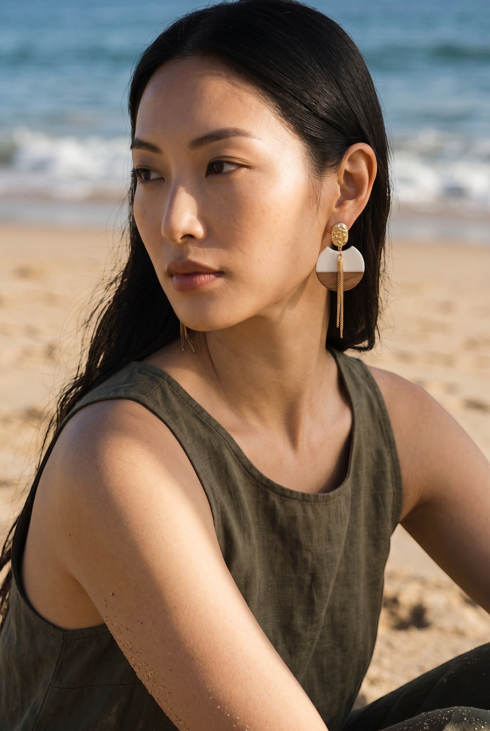 Sand and Sea geometric wood and gold metal drop earrings with chain detail on a model at the beach.