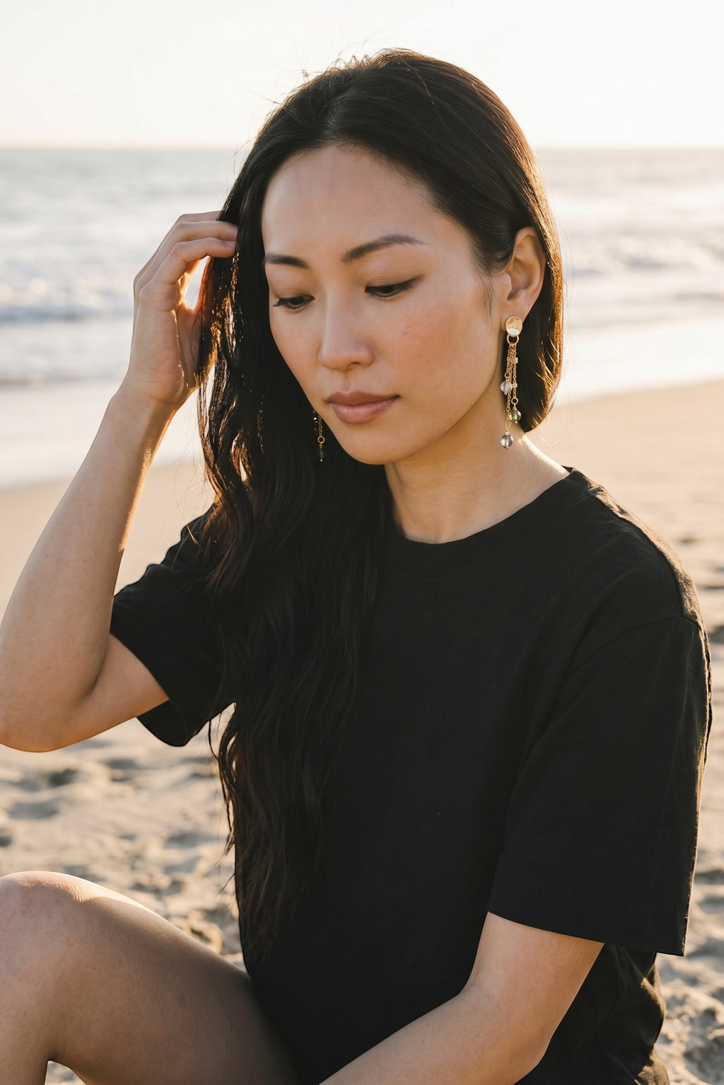 Sand and Sea gold plated drop earrings with pastel beads and gold chain, worn by a woman on the beach.