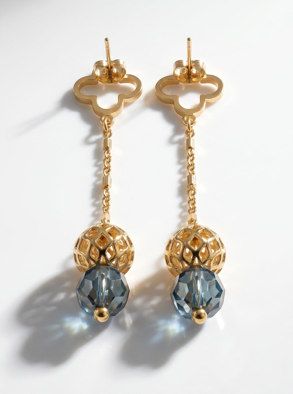 Sand and Sea gold-tone drop earrings with clover stud, chain, and faceted blue gemstone.