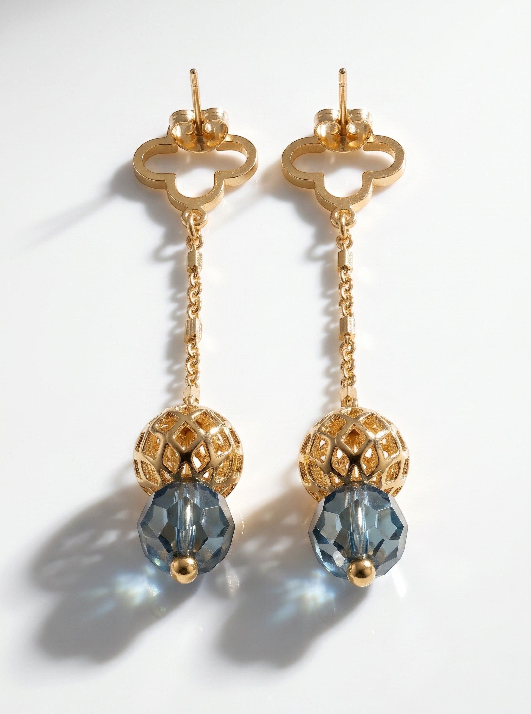 Sand and Sea gold-tone drop earrings with clover stud, chain, and faceted blue gemstone.