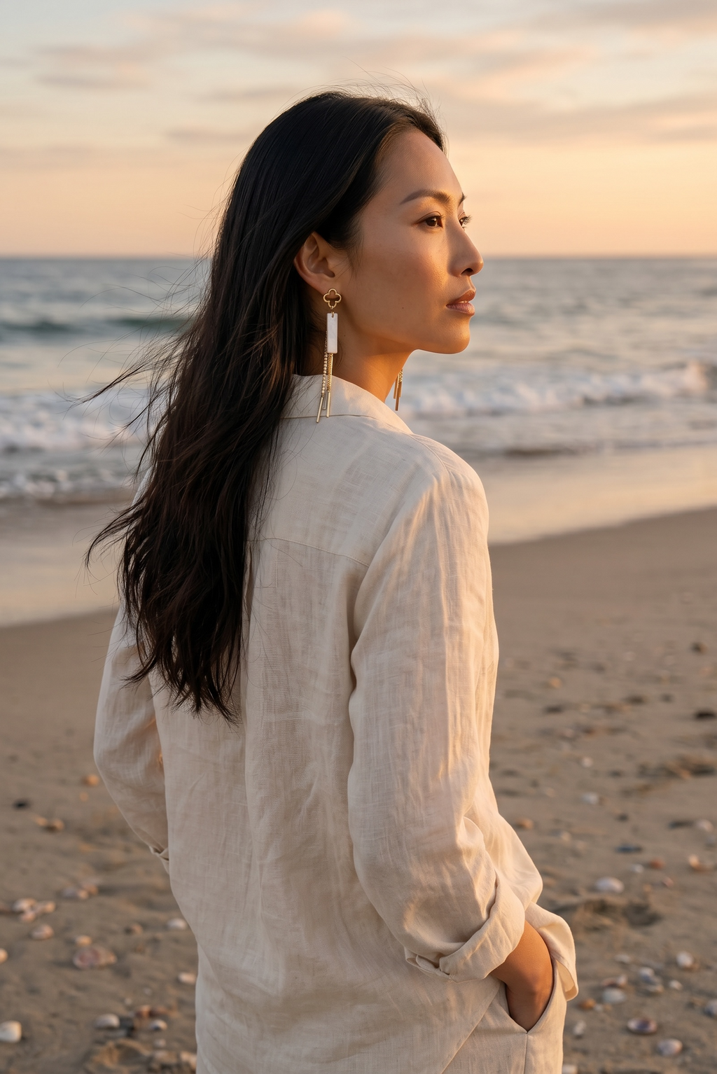 Sand and Sea gold clover dangle earrings with white stone and chains on a woman at the beach.