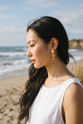 Sand and Sea gold-plated dangle earrings with quatrefoil charm, princess-cut cubic zirconia, and blue-green teardrop bead.