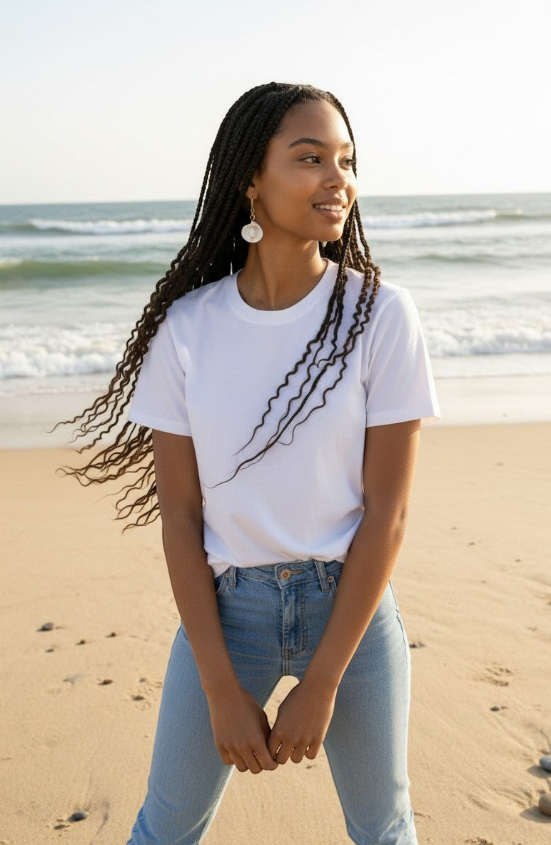 Sand and Sea 18k gold dangle earrings with white shell and pearl accents on a model at the beach.