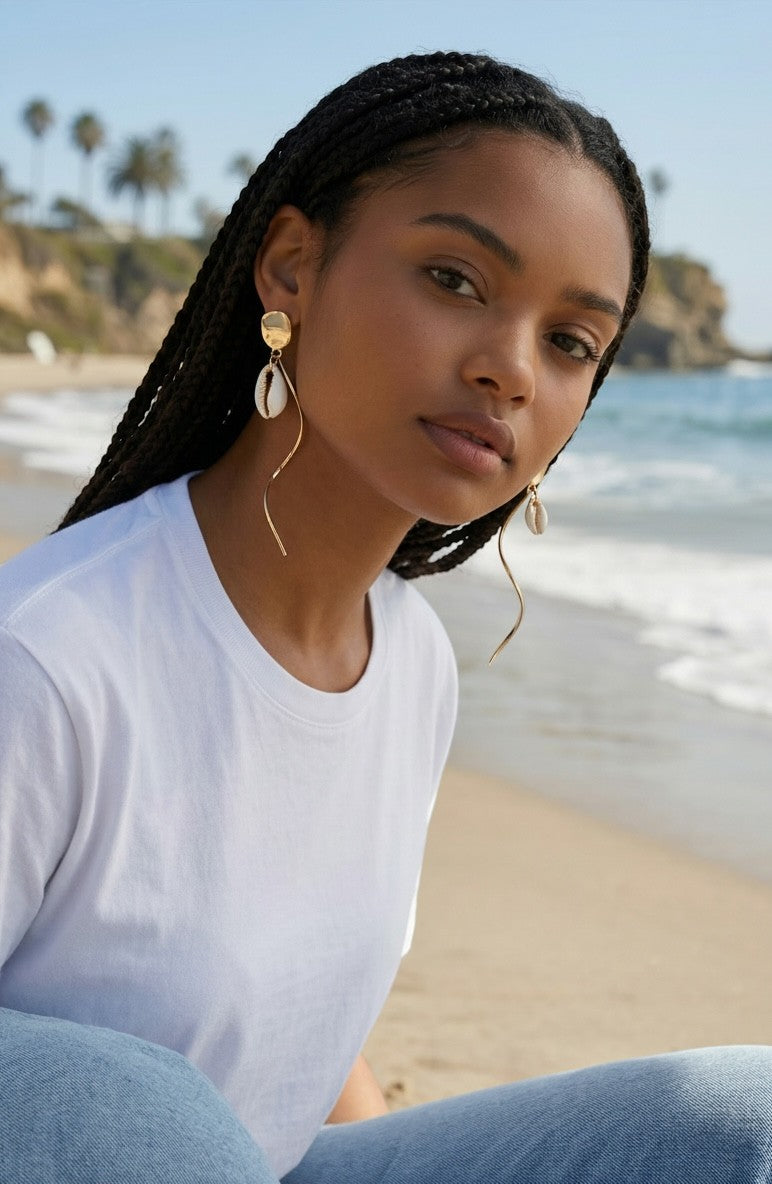 Sand and Sea 18k gold twisted post dangle earrings with white shell accents on a model at the beach.