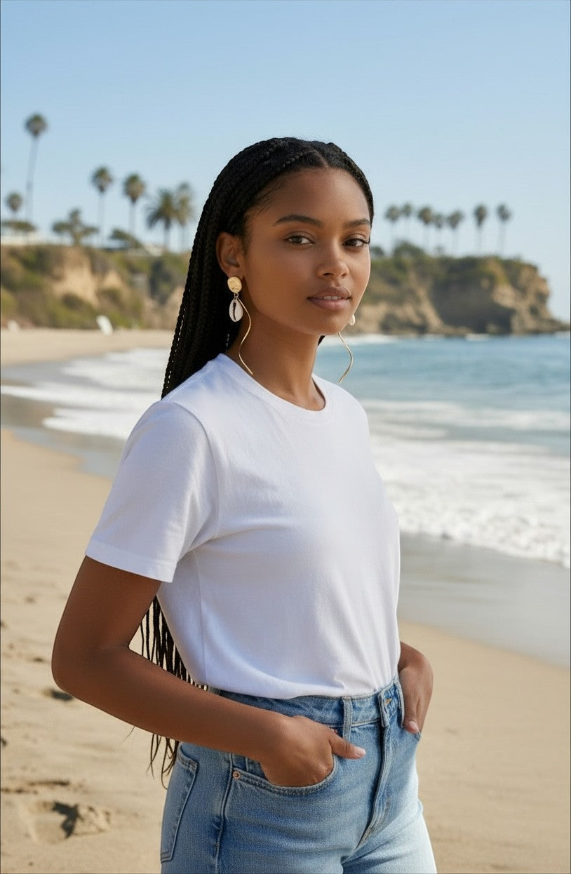 Sand and Sea 18k gold twisted post earrings with white shell dangle on a woman at the beach.