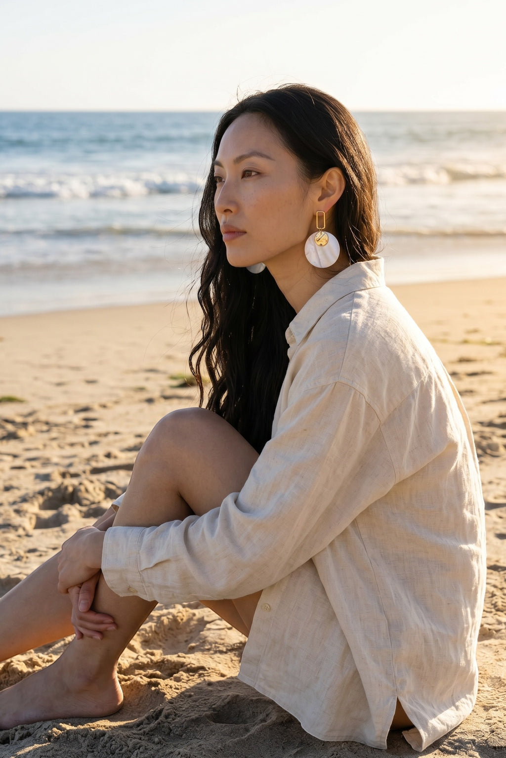 Sand and Sea white and cream marbled disc earrings with gold rectangular frame on model at beach.