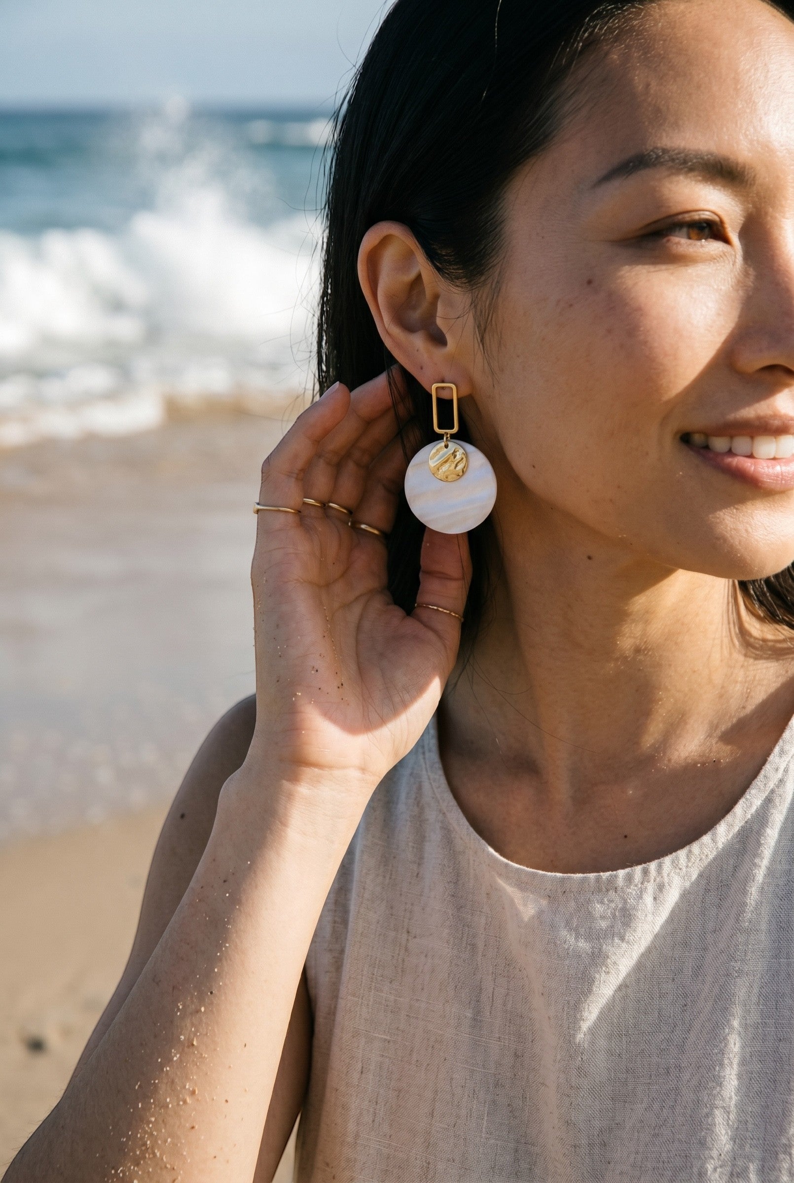 Sand and Sea white and cream marbled disc earrings with gold rectangular frame. Model on beach.