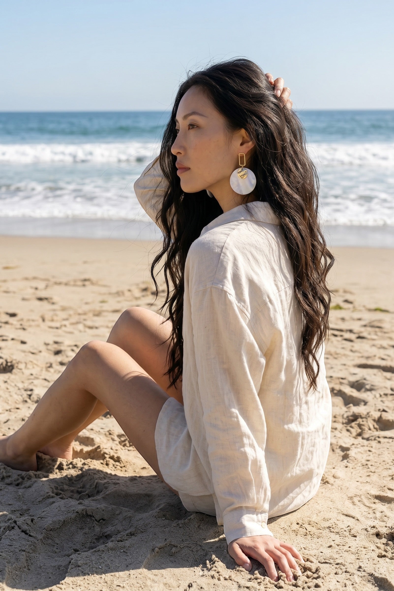 Sand and Sea white and cream marbled disc earrings with gold rectangular frame, worn by a woman on the beach.
