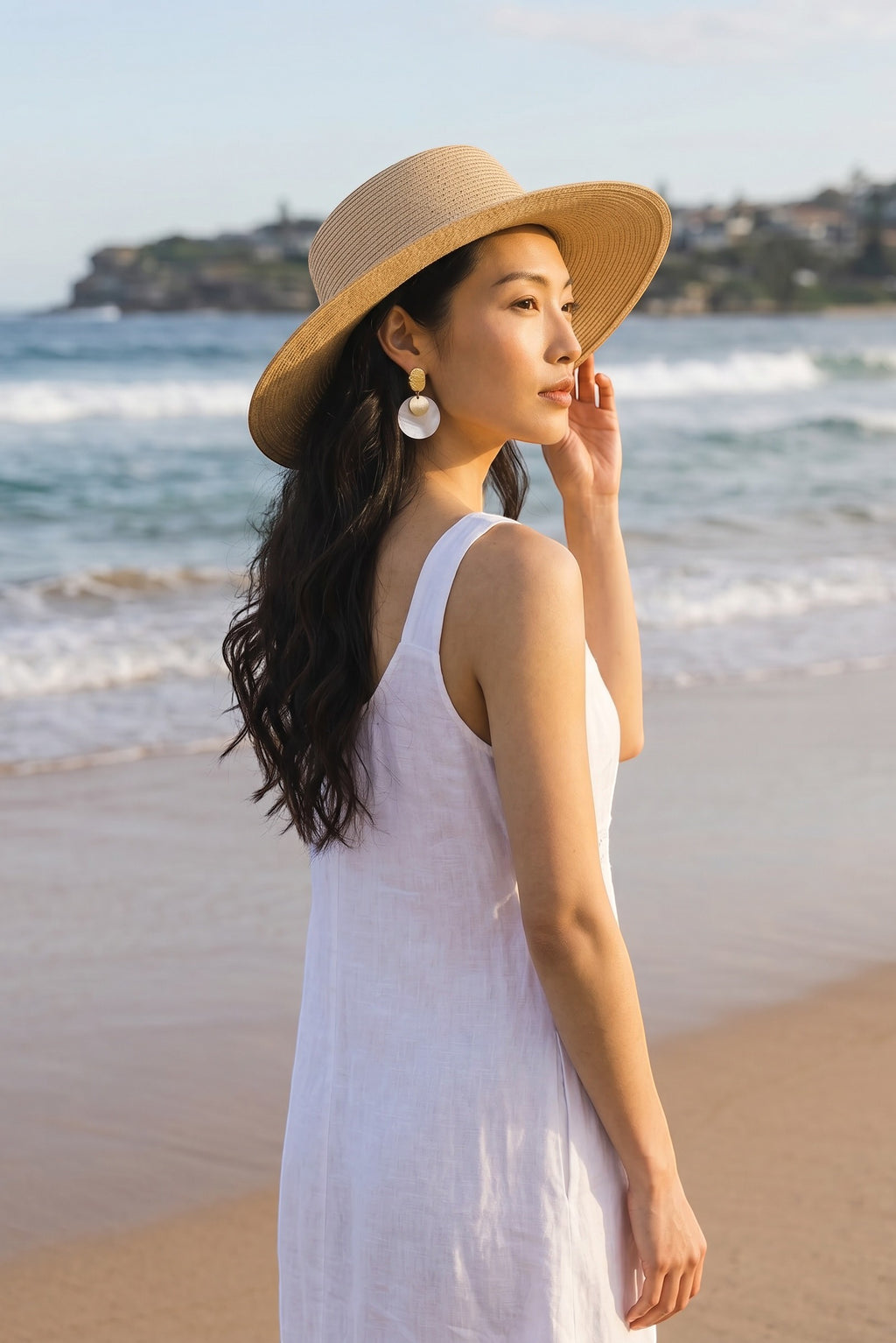 Sand and Sea gold accent round disc shell earrings on a woman at the beach.