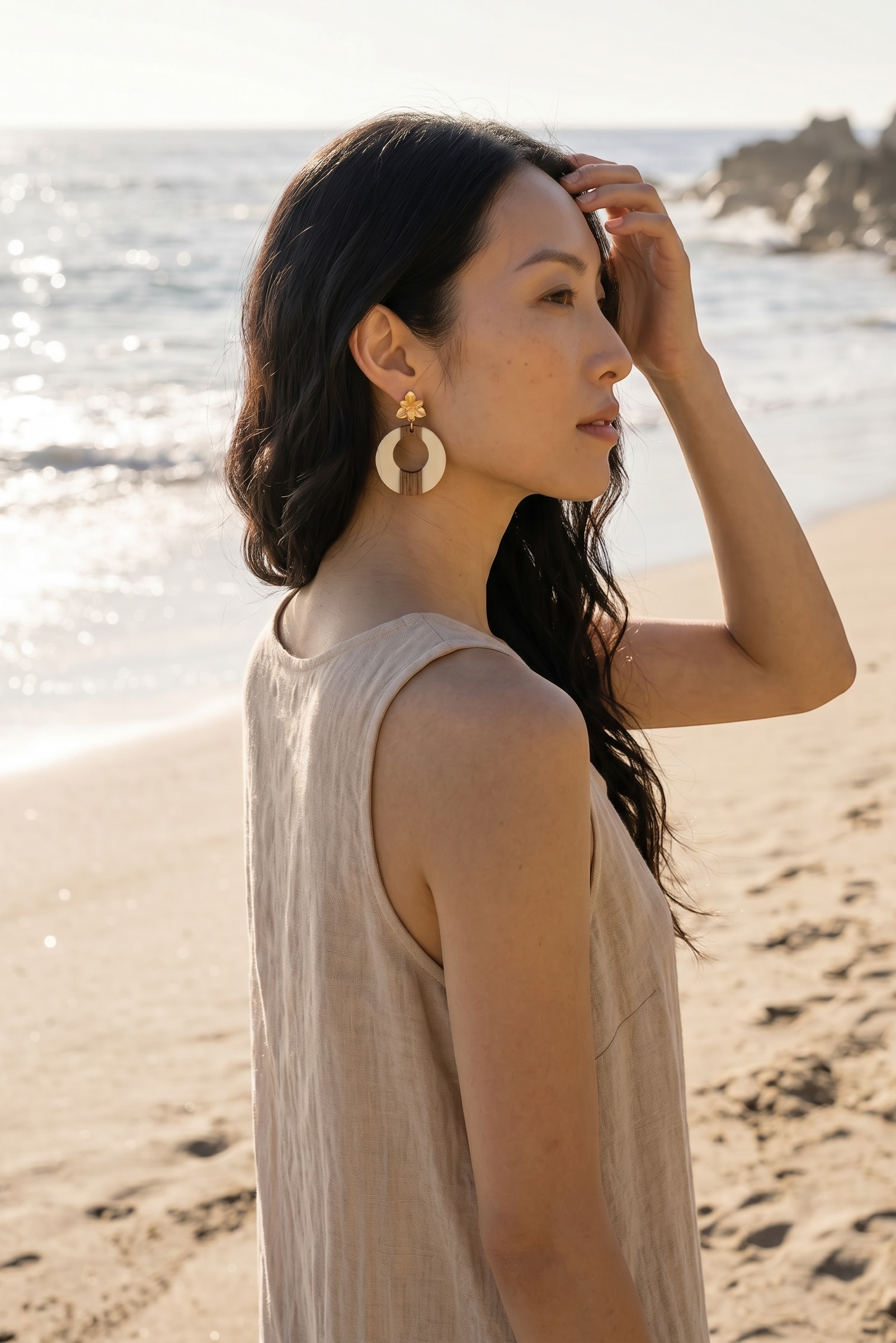Sand and Sea statement hoop earrings with wood and cream accents, featuring a floral stud. Model on beach.