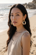 Sand and Sea statement hoop earrings with wood and cream accents and floral stud, worn by a model on a beach.