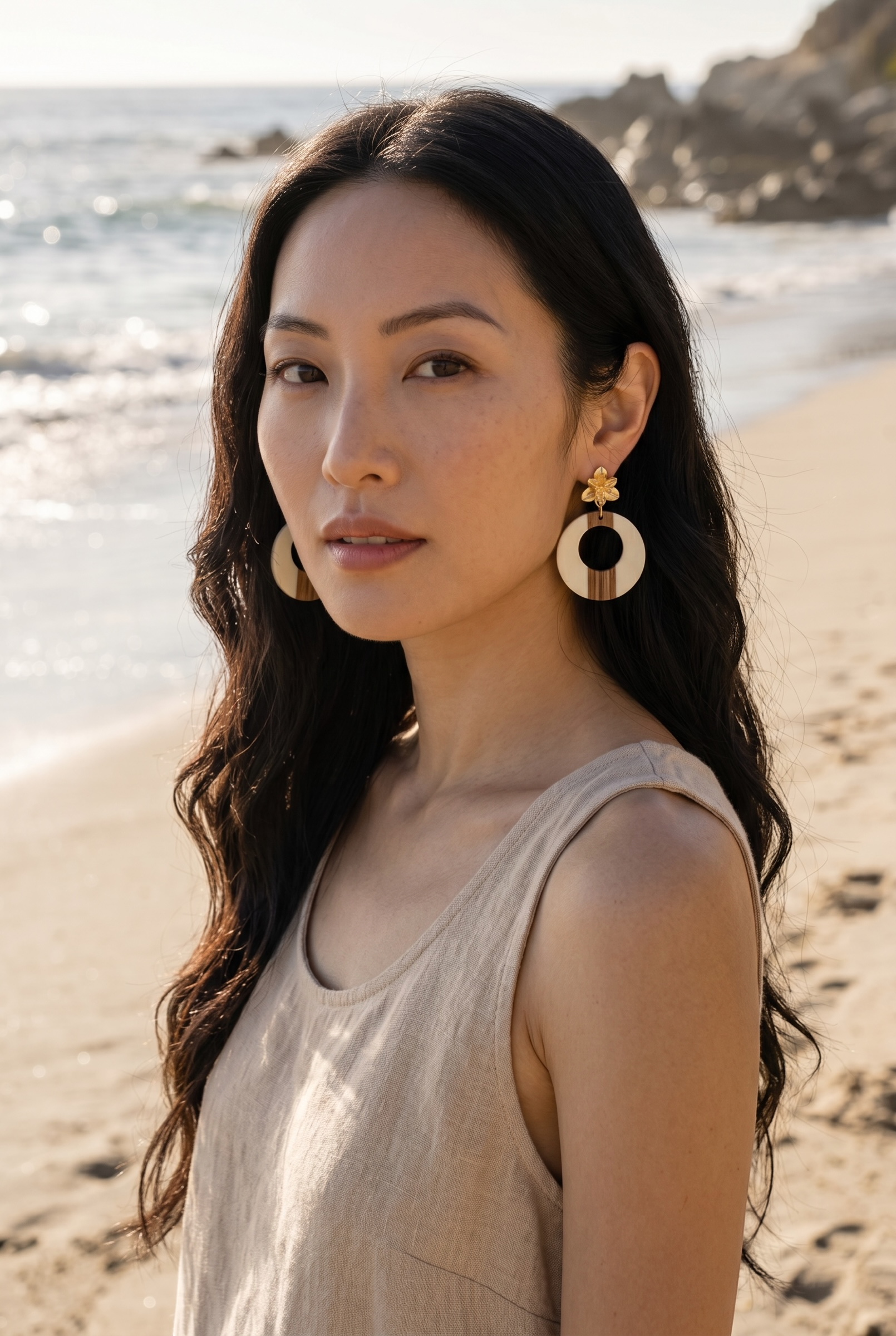 Sand and Sea statement hoop earrings with wood and cream accents and floral stud, worn by a model on a beach.